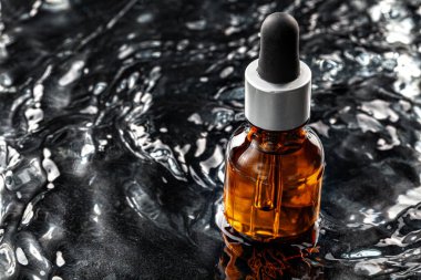 Cilt bakımı, siyah dalgalı suda serum şişesi.