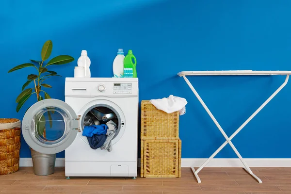 Washing machine with laundry on blue wall background — Stock Photo, Image
