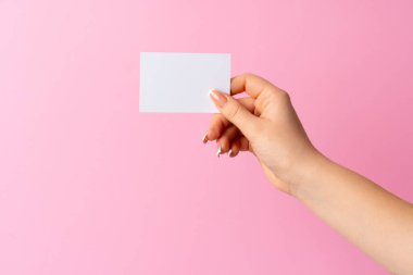 Pembe arka planda boş kartvizit gösteren kadın eli.
