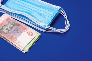 Tıbbi yüz maskesi ve mavi arka planda Ukrayna Hryvnia banknotları