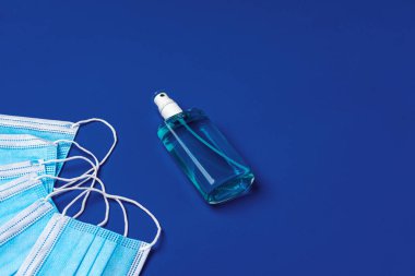 Mavi arka planda el dezenfektanı olan bir yığın tıbbi yüz maskesi.