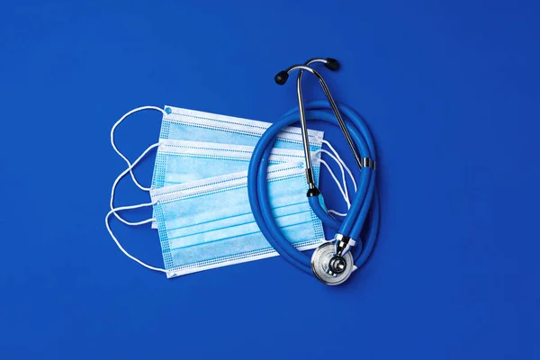 Medical face masks and stethoscope on blue background
