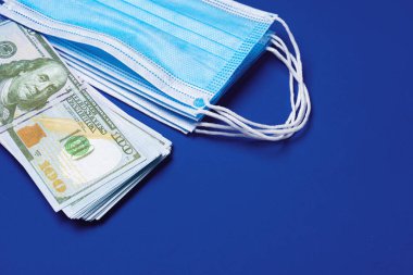 Mavi arka planda tıbbi koruyucu maskeler ve Amerikan doları banknotlarını kapatın.
