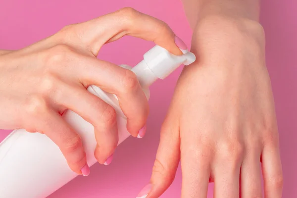 Mão feminina segurando garrafa de produto skincare em rosa — Fotografia de Stock
