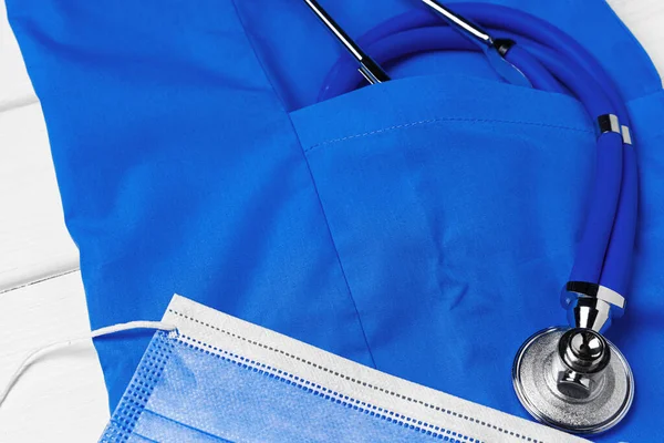 Médico médico uniforme con estetoscopio y mascarilla sobre fondo de madera blanco — Foto de Stock