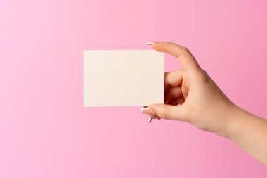 Pembe arka planda boş kartvizit gösteren kadın eli.