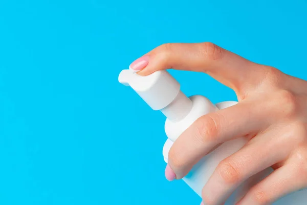Vrouwelijke hand houden huidverzorgingsproduct fles op blauw — Stockfoto