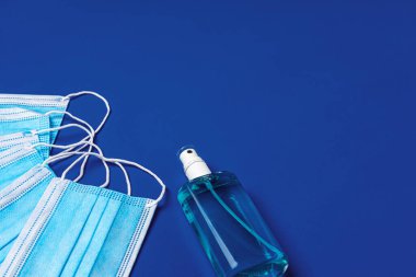 Mavi arka planda el dezenfektanı olan bir yığın tıbbi yüz maskesi.