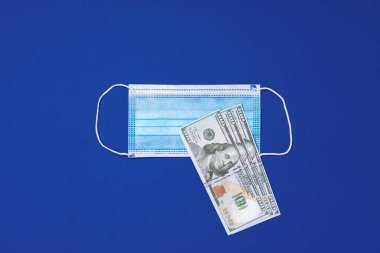 Mavi arka planda tıbbi koruyucu maskeler ve Amerikan doları banknotlarını kapatın.