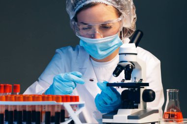 Laboratuvarda mikroskop yakınında kan örneği olan bir kadın bilim adamı incelemesi yapıyor.