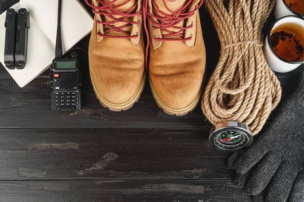 Hiking boots with equipment for hiking, cup of tea on wooden board — Stock Photo, Image