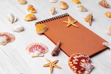 Tahta levhaların üzerinde deniz kabukları olan kahverengi not defterinin yakın plan fotoğrafını çek.