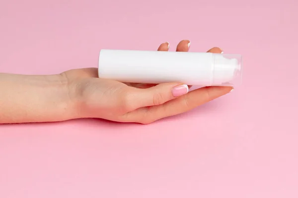 Mão feminina segurando garrafa de produto skincare em rosa — Fotografia de Stock