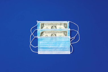 Mavi arka planda tıbbi koruyucu maskeler ve Amerikan doları banknotlarını kapatın.