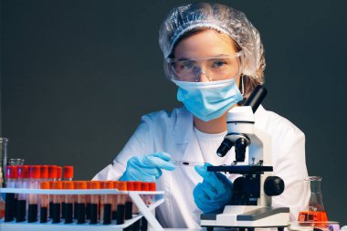 Laboratuvarda mikroskop yakınında kan örneği olan bir kadın bilim adamı incelemesi yapıyor.