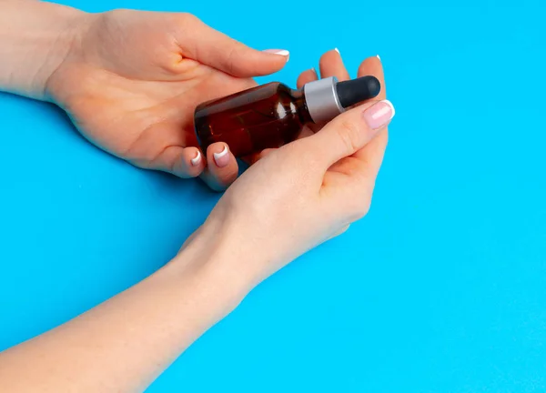 Botella de producto de cuidado de la piel de mano femenina en azul — Foto de Stock