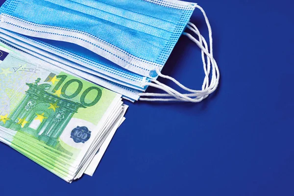 Купа масок для медичного обличчя та банкноти євро на синьому фоні. — стокове фото