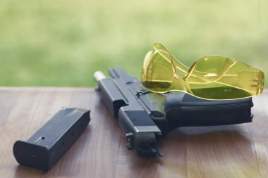 Handgun with safety glasses on a wooden background. clipart