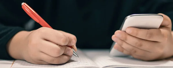 Close up van jonge student met smartphone schrijven naar laptop. — Stockfoto