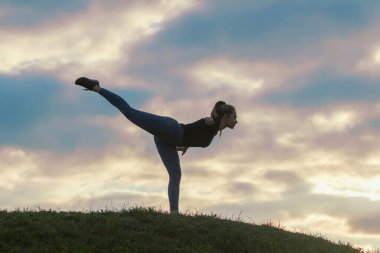 Genç kadının tek ayak üstünde duran ve üzerinde çim sabah egzersiz