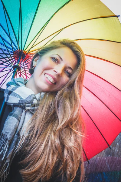 Uzun saçlı bir parlak renkli şemsiye altında duran ve gülümseyen güzel genç kız — Stok fotoğraf