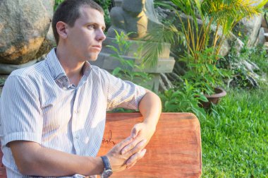 Bir gömlek, şort ve saat bankta oturmak rahat çekici gülümseyen adam