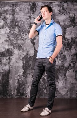 Yakışıklı genç adam resmi kıyafeti içinde büyüleyici konuşurken telefon, lwhile ayakta, gri arka plan üzerinde