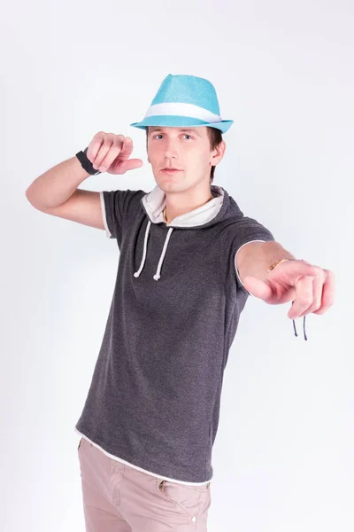 Encantador joven guapo en formalwear sostiene sus manos, sombrero azul señala con los dedos a la cámara, fondo blanco — Foto de Stock