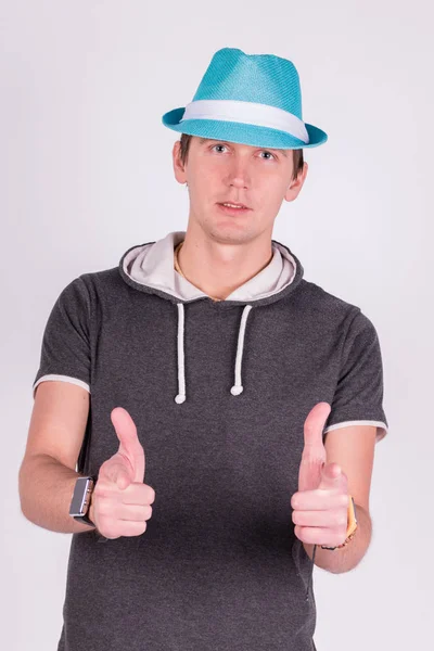 Encantador joven guapo en formalwear puntos con los dedos, Levantado, lux en la cámara Sombrero azul, fondo blanco — Foto de Stock