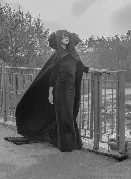 La imagen de Halloween chica bonita en un vestido y máscara caminando a través del puente en blanco y negro . —  Fotos de Stock