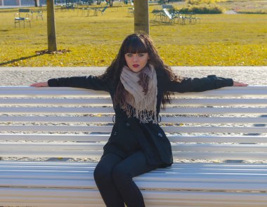 bir Park bankında bir kız siyah bir ceket oturuyor.