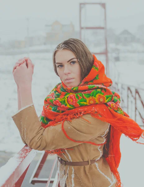 Beautiful girl in a scarf in the winter stands on the bridge holding onto the railing. — Stock Photo, Image