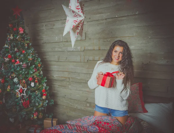 Приваблива дівчина в білому светрі розпаковує різдвяні подарунки в ліжку . — стокове фото