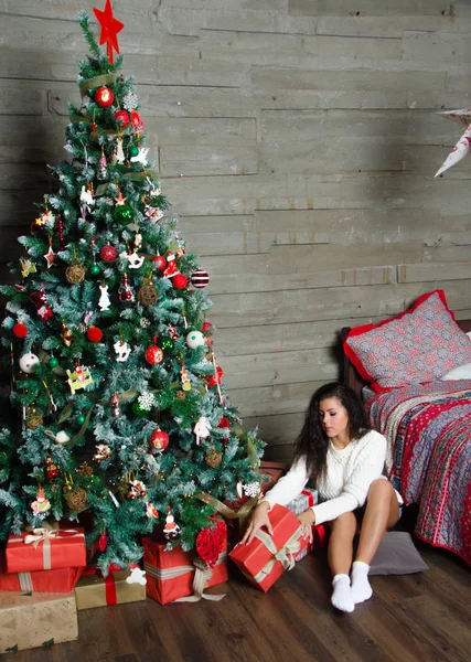 La chica en el suéter blanco sentado cerca del árbol de Navidad parses regalos . — Foto de Stock