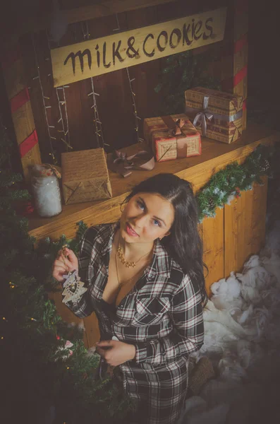 Schöne Mädchen in kariertem Hemd in der Nähe der Theke Milch und Plätzchen kleidet Weihnachtsbaum. — Stockfoto