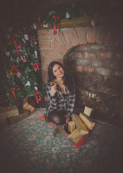 Hermosa chica en camisa a cuadros con una copa de vino en Navidad quiere romper la chimenea — Foto de Stock