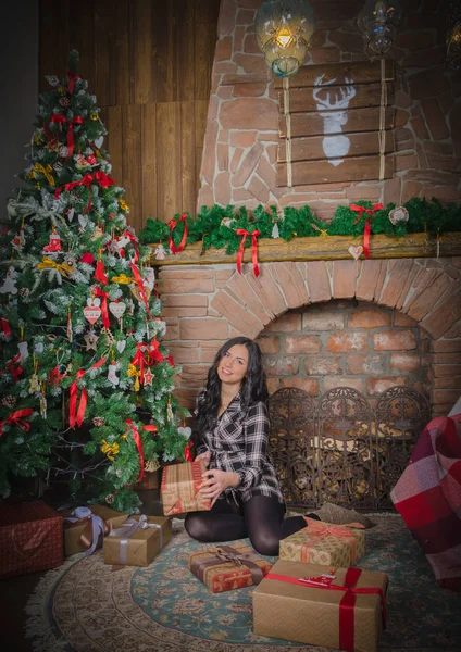 Navidad hermosa chica sentada cerca de la chimenea y regocijarse en los regalos . — Foto de Stock