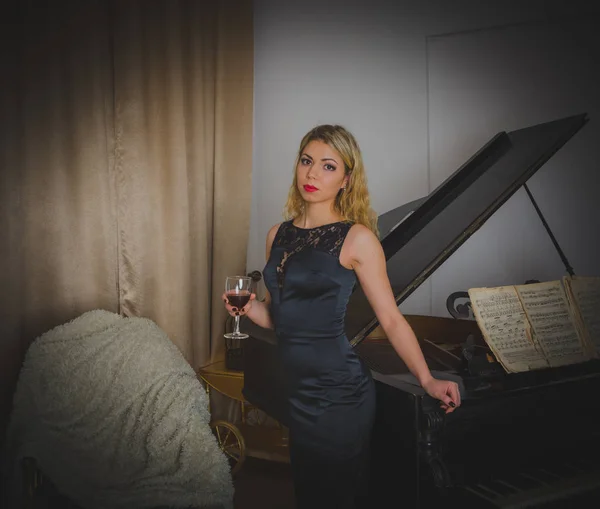 Ένα ποτήρι κρασί, ένα ελκυστικό κορίτσι σε ένα μαύρο φόρεμα το πιάνο με τις σημειώσεις. — Φωτογραφία Αρχείου