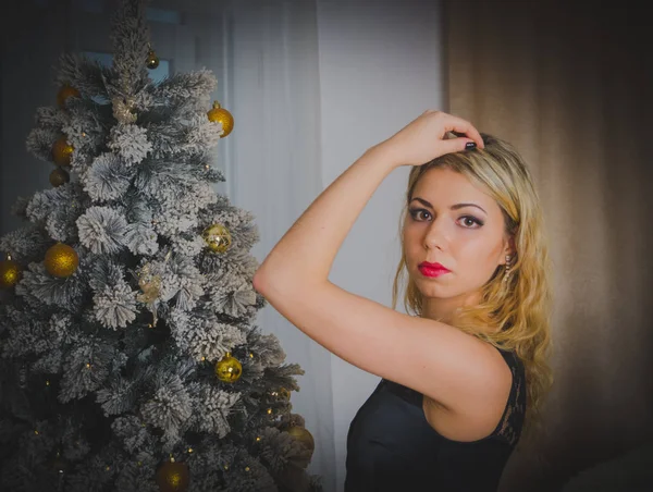 In der Nähe des Weihnachtsbaums posiert schönes Mädchen in schwarzem Kleid. — Stockfoto