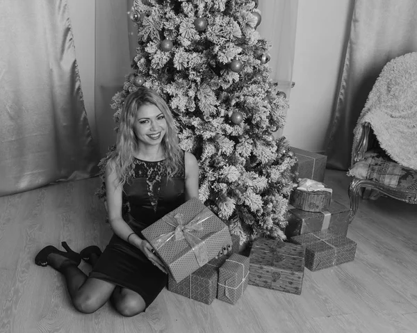 Schönes Mädchen in schwarzem Kleid am Abend sitzt ein Weihnachtsbaum am Geschenk, schwarz weiß. — Stockfoto