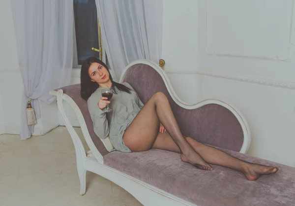 En attraktiv tjej i en t-shirt som ligger på soffan med ett glas vin. — Stockfoto