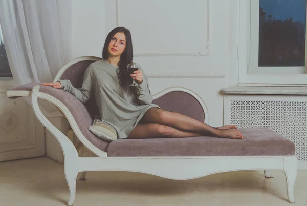 Com um copo de vinho no sofá menina bonita em t-shirt . — Fotografia de Stock