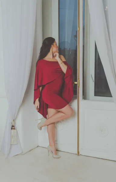 De pé na janela uma menina bonita em um vestido vermelho — Fotografia de Stock