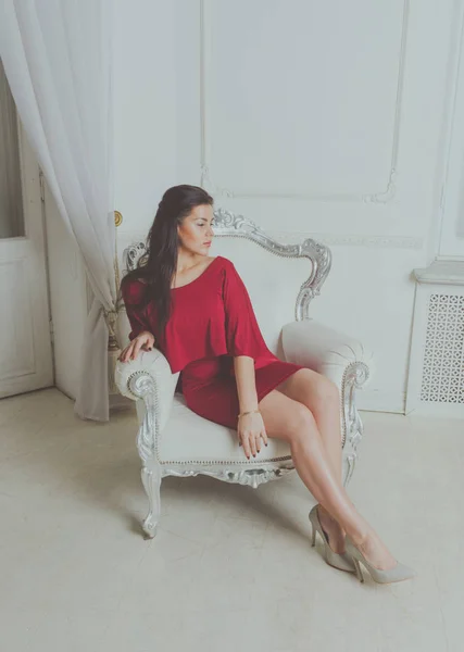 Vintage sandalye çekici bir kız kırmızı bir elbise içinde oturur. — Stok fotoğraf