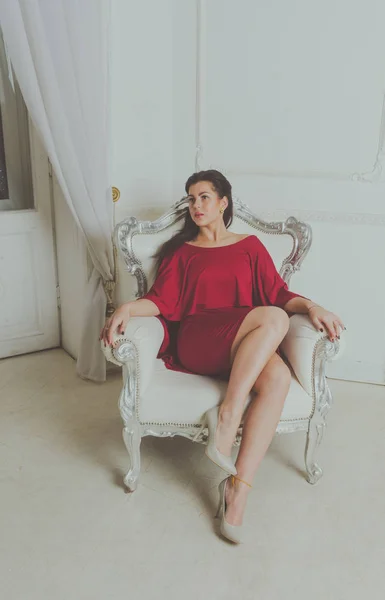 Όμορφο κορίτσι με κόκκινο φόρεμα που θέτουν σε μια vintage καρέκλα. — Φωτογραφία Αρχείου