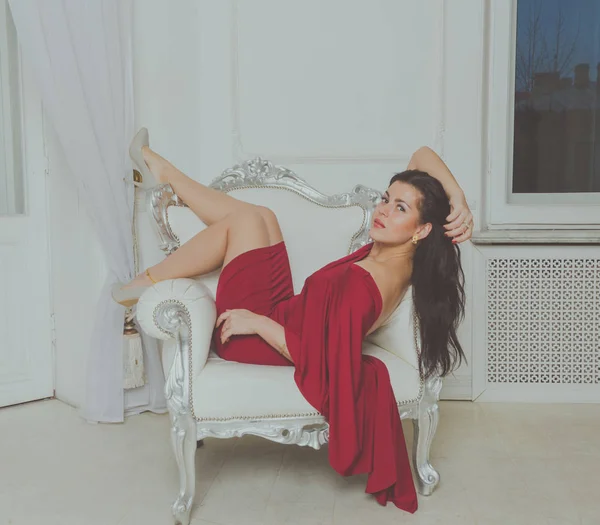 Le gambe su una sedia vintage, una ragazza attraente con un vestito rosso . — Foto Stock