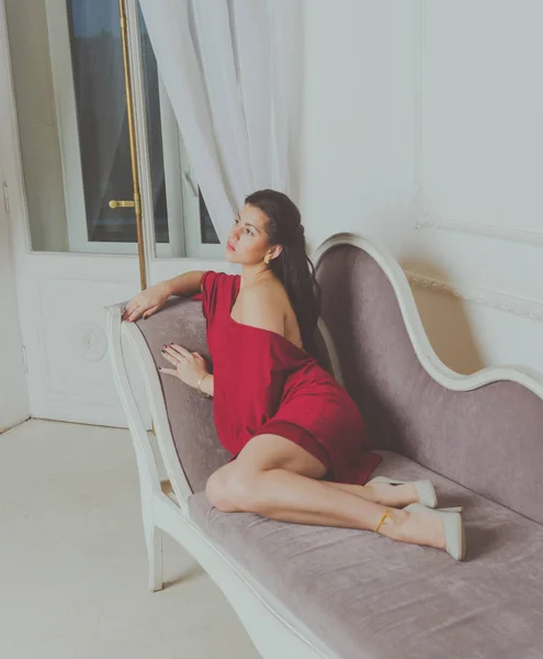 Chica atractiva en vestido rojo posando en el sofá —  Fotos de Stock