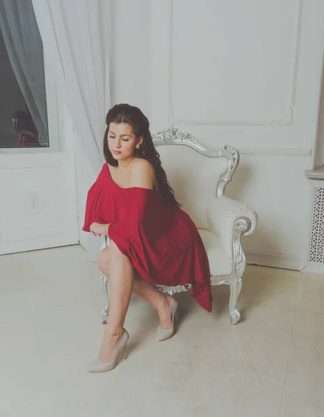 Красива дівчина в червоній сукні Зачистки-плечі в вінтажному кріслі . — стокове фото