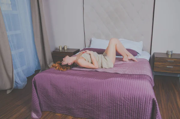 Ενδιαφέρουσα κορίτσι σε ένα φόρεμα στο κρεβάτι στο δωμάτιο του ξενοδοχείου — Φωτογραφία Αρχείου