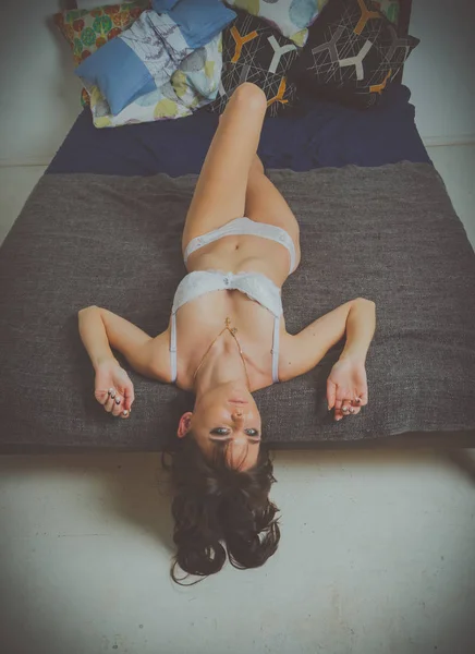 Ποζάρει και βλέπουν φωτογραφική μηχανή, ξαπλωμένη στο κρεβάτι σέξι κορίτσι στο λευκό εσώρουχα — Φωτογραφία Αρχείου